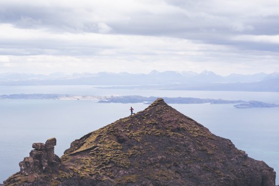 A trail runner races along a ridge on a rugged coastal landscape.