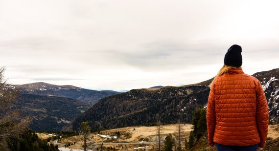 Frau mit roter Jacke blickt in die Ferne mit Bergpanorama