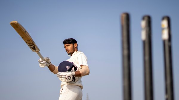 An Indian cricketer holds a helmet and bat.