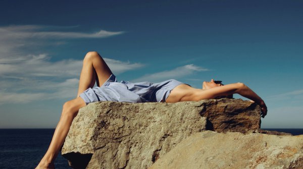 A woman sunbathing on a rocky coast.