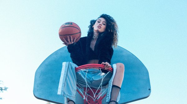 Woman sitting in the basketball hoop and holding a basketball